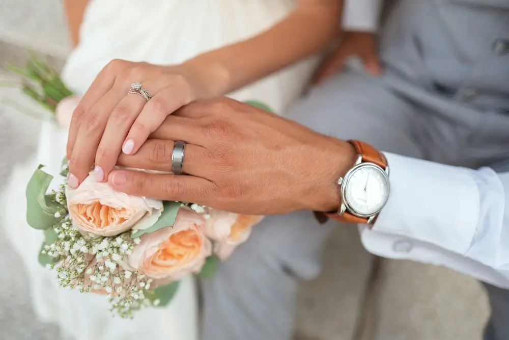 Two hands with wedding rings over a bouquet of peach roses